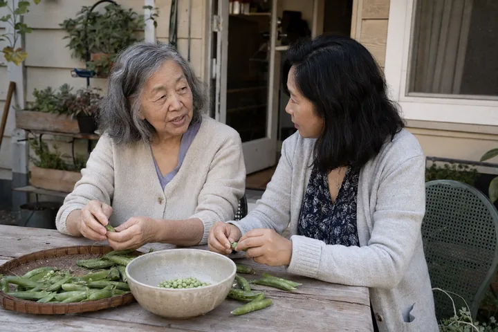 An older woman and her adult daughter preparing peas together on a porch